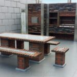 Aménagement moderne d'une cuisine extérieure en briques rouges et pierres sombres avec four à pizza, barbecue intégré et table de jardin assortie