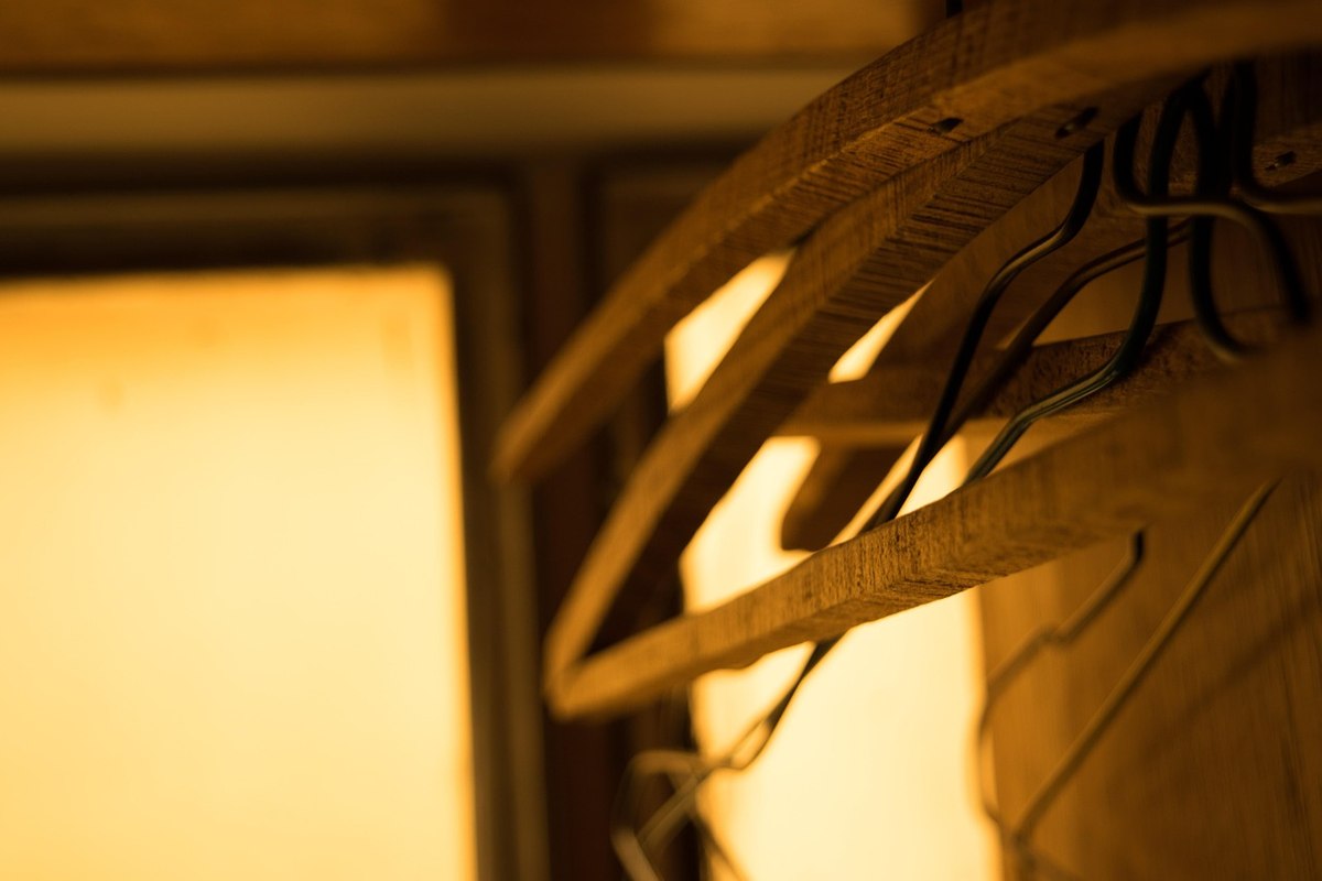 Des cintres en bois accrochés à un support près d'une fenêtre éclairée Des cintres en bois accrochés à un support près d'une fenêtre éclairée