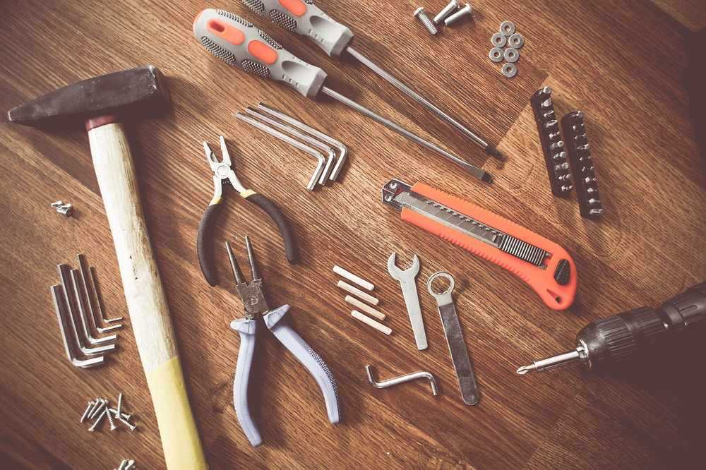 Outils de bricolage sur une surface en bois, avec des pinces, des tournevis, une lime, des clous et des vis