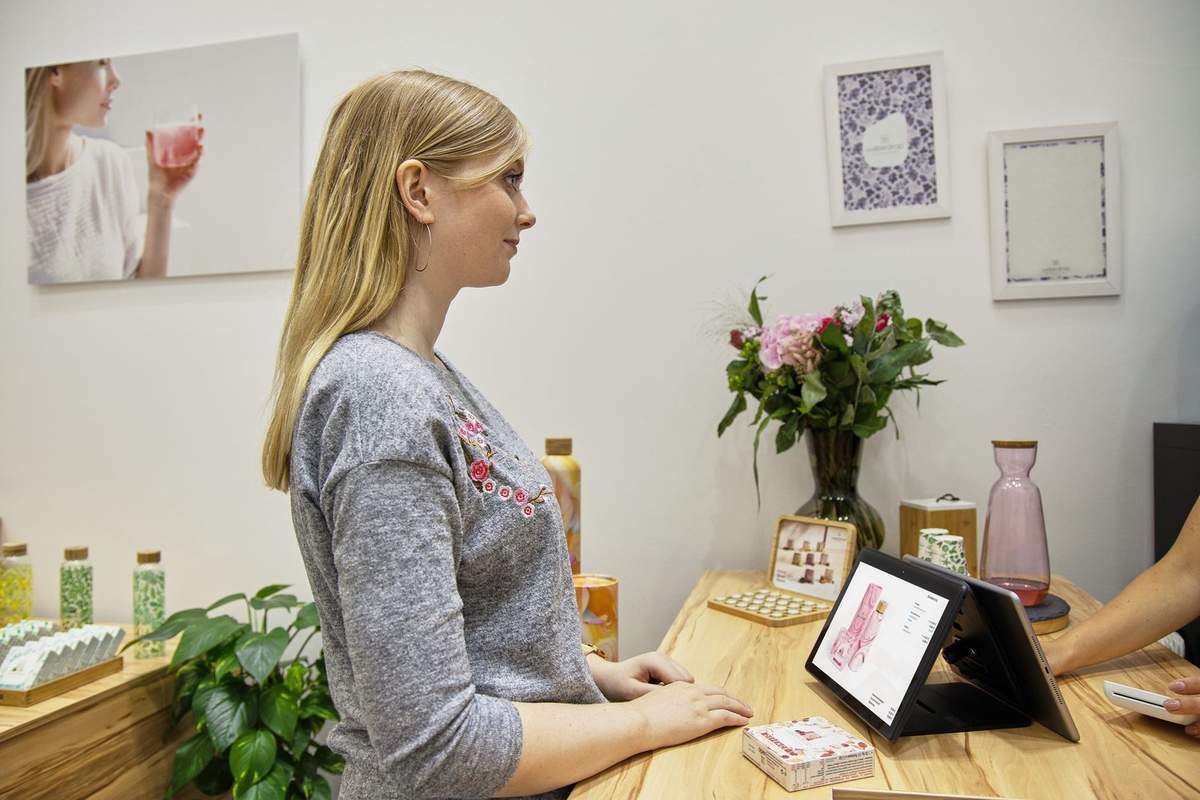 Femme blonde en gris devant un écran de caisse dans un salon décoré Femme blonde en gris devant un écran de caisse dans un salon décoré
