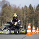 Un coureur en casque pilote un kart sur un circuit avec cônes
