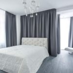 Une chambre moderne avec lit, chaise, rideaux gris et lustre