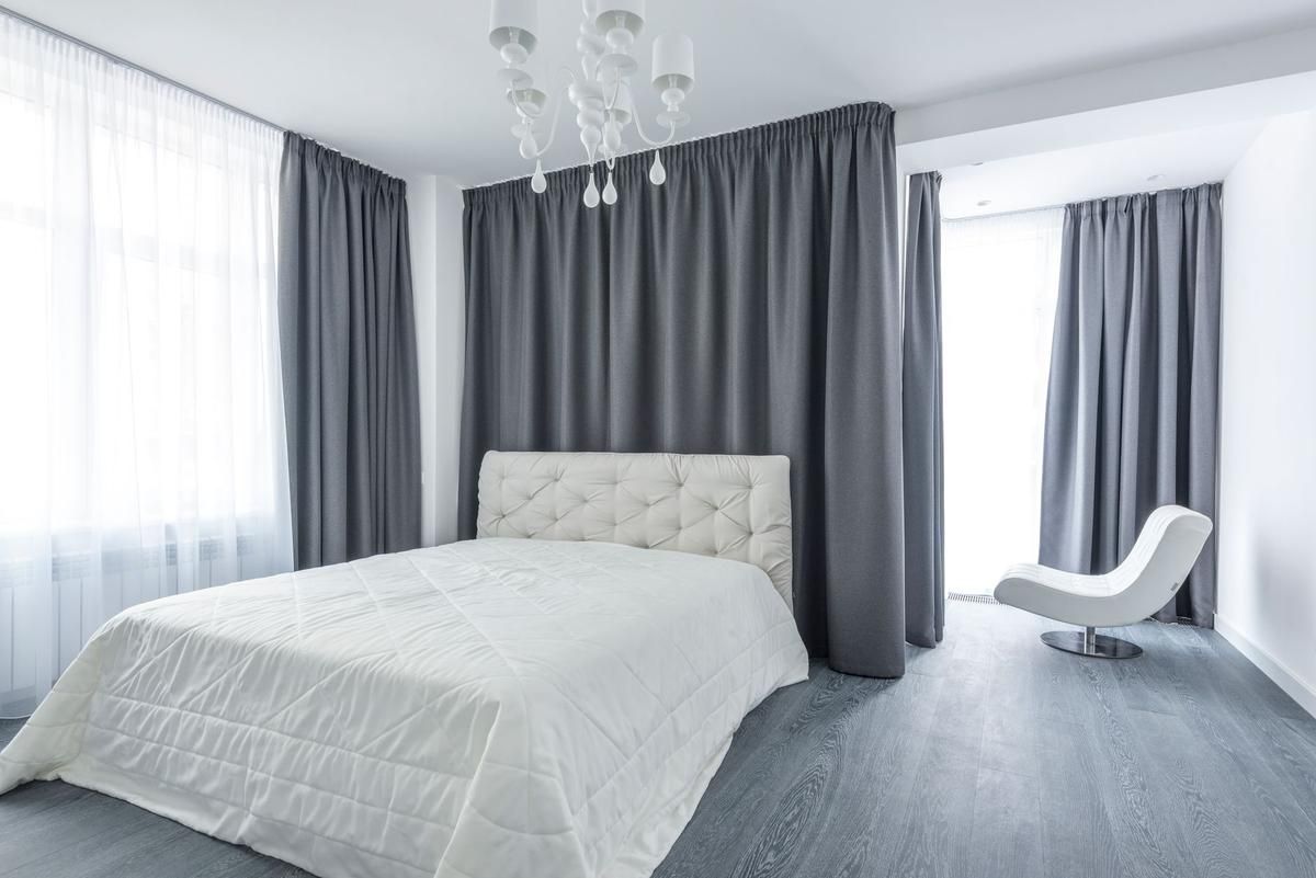 Une chambre moderne avec lit, chaise, rideaux gris et lustre